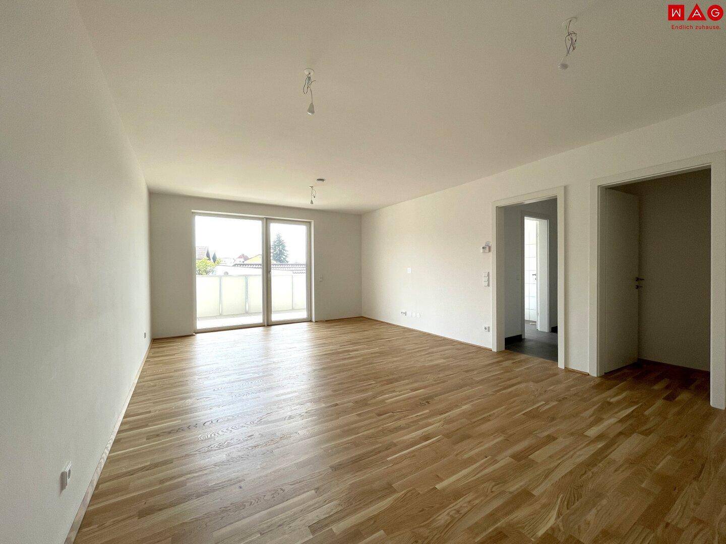 Geräumiger Wohn-Essbereich mit hellem Eichenparkettboden und großen Fenstern mit Zugang zum Balkon.