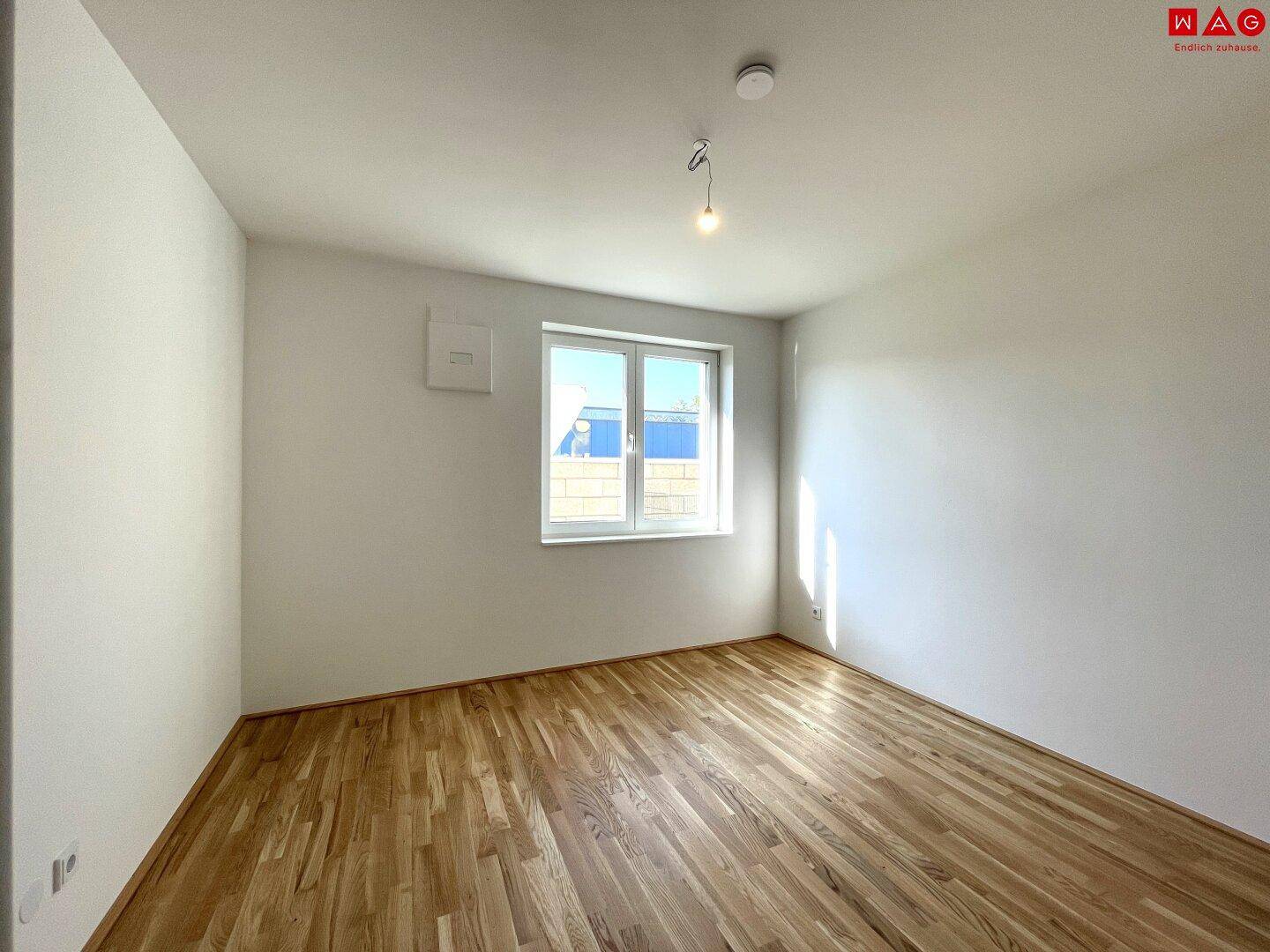 Leeres Schlafzimmer mit Holzboden und einem Fenster, das viel Tageslicht hereinlässt.
