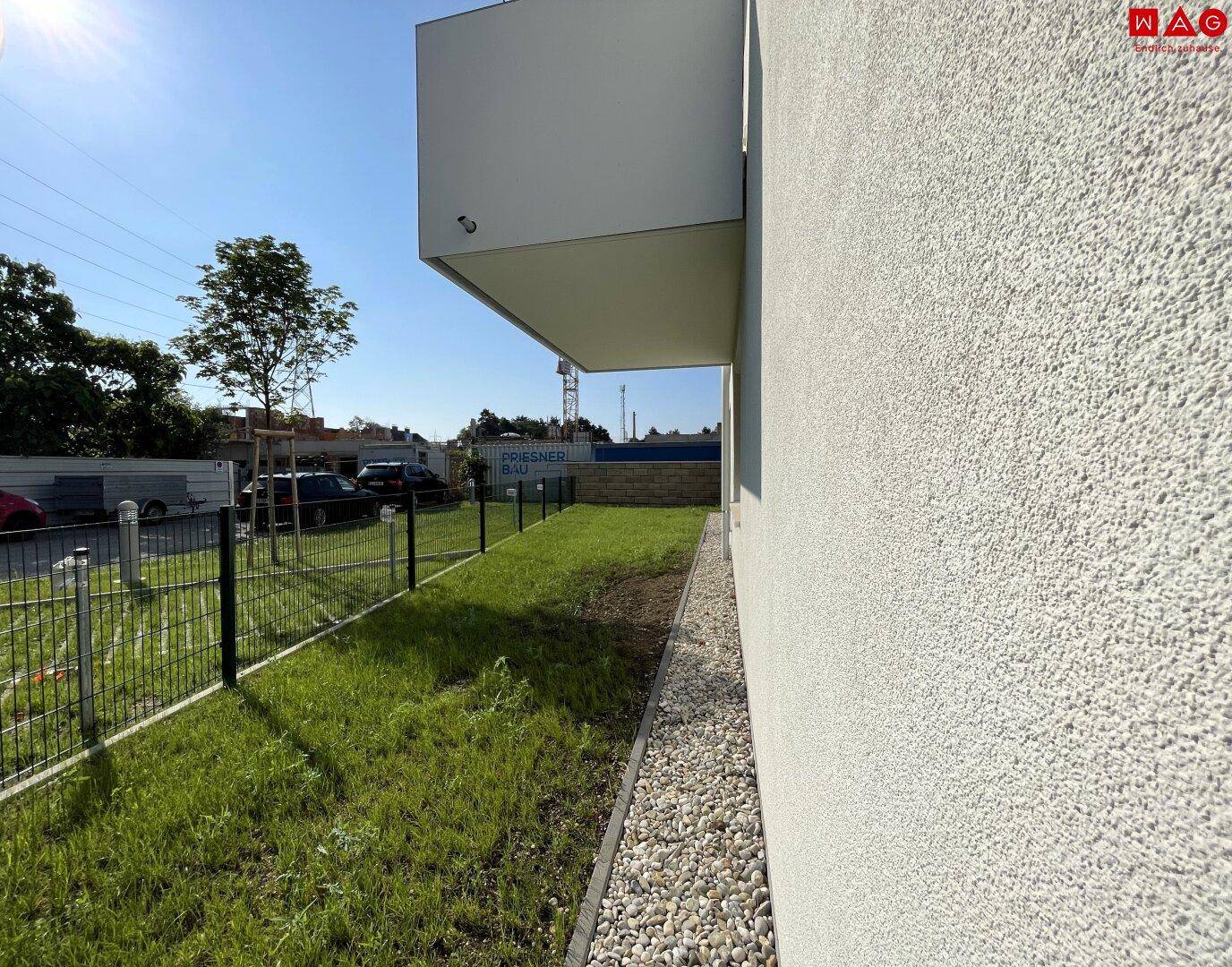Seitenansicht eines Neubaus mit Rasenfläche und Kiesstreifen entlang der Fassade.