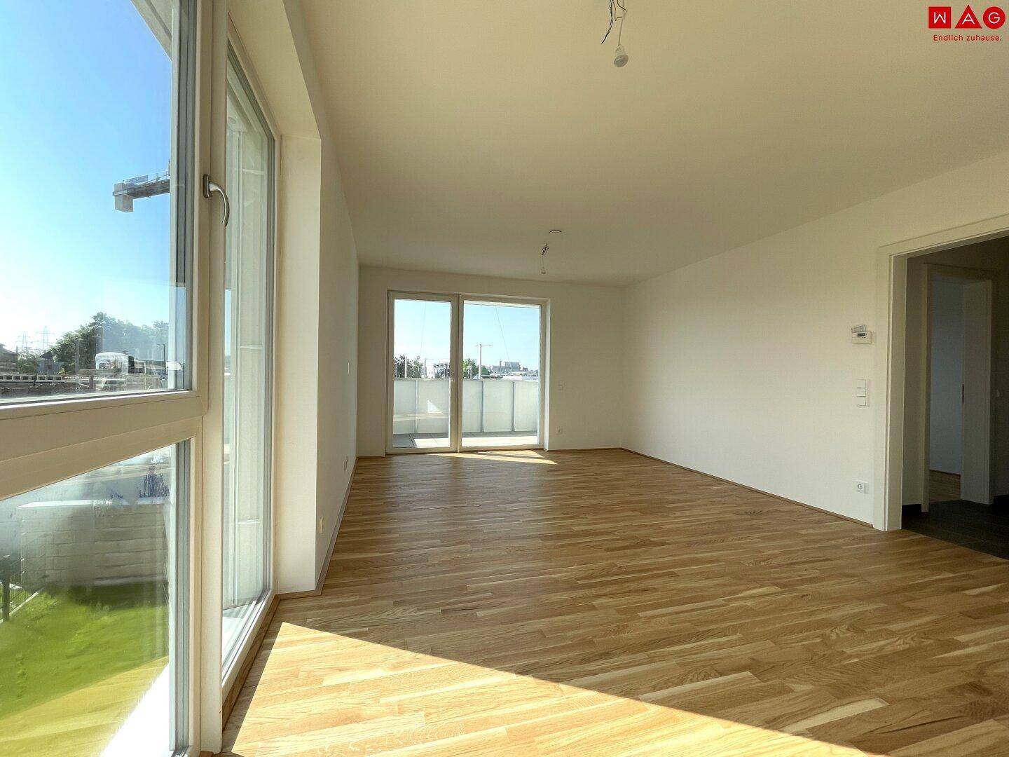 Geräumiges, unmöbliertes Wohnzimmer mit hellem Holzboden und großen Fenstern.