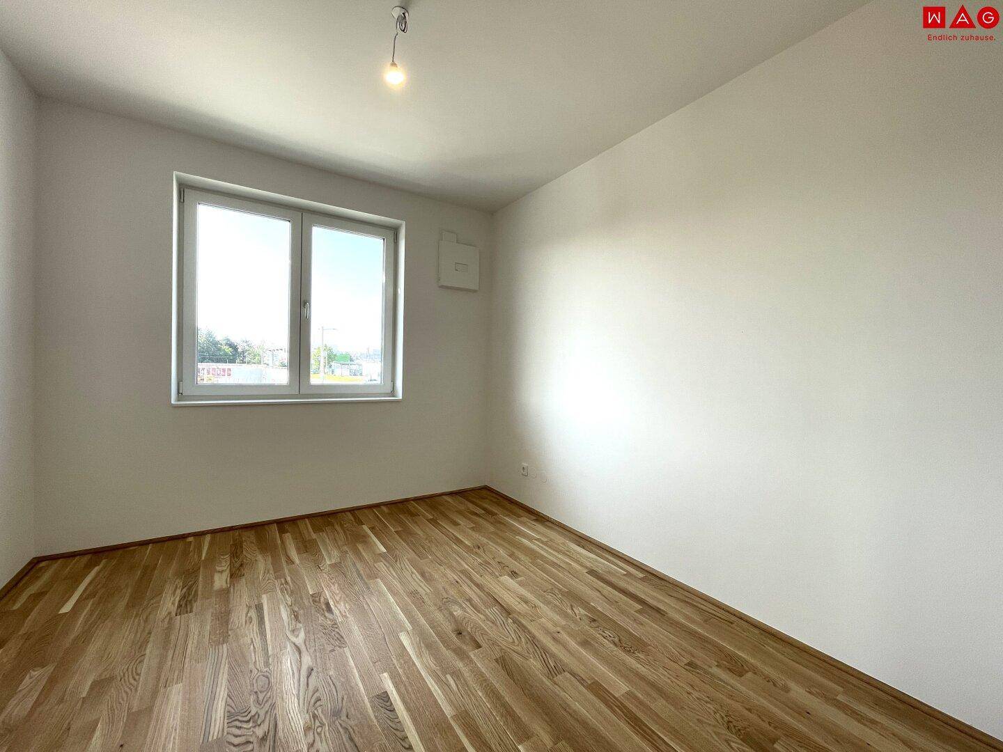 Geräumiges, unmöbliertes Schlafzimmer mit Holzboden und Fenster.