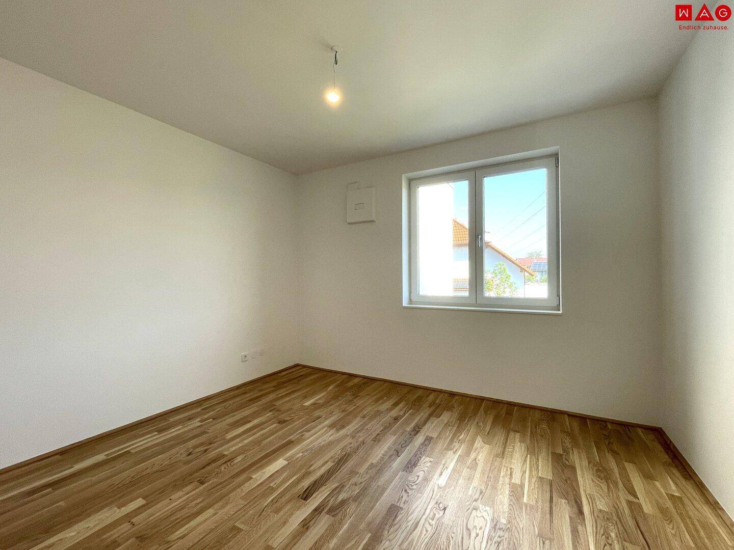 Leeres Zimmer mit Holzboden und Fenster, ideal als Schlafzimmer oder Gästezimmer nutzbar.