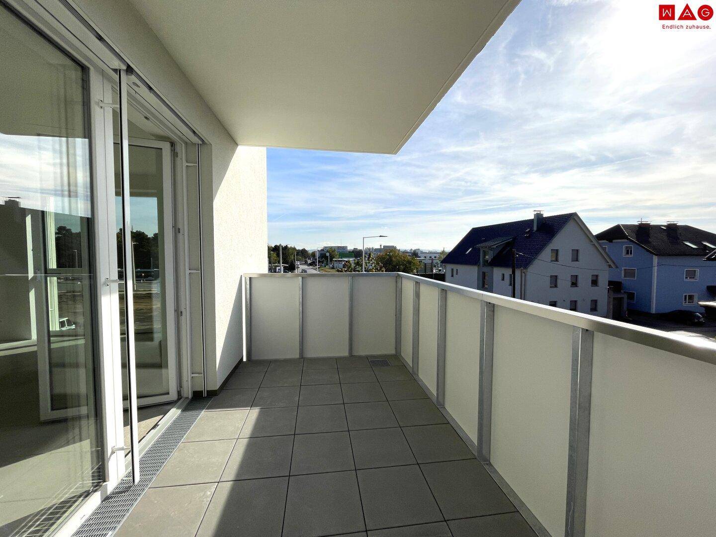 Heller Balkon mit Fliesenboden und Blick auf die Straße sowie benachbarte Gebäude.