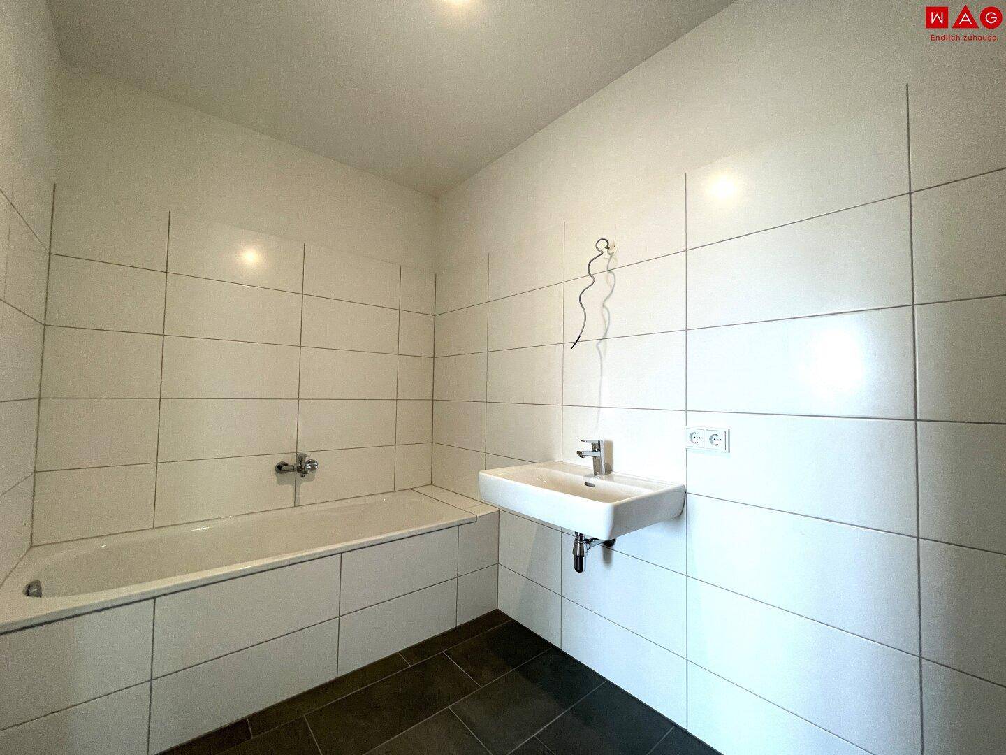 Helles Badezimmer mit Badewanne, Einzelwaschbecken und weißen Wandfliesen.