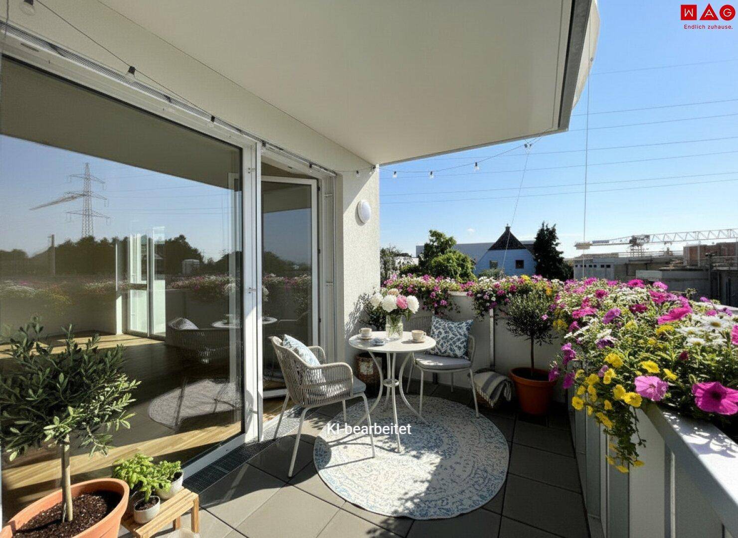 Sonniger Balkon mit Gartenmöbeln, vielen Blumen und Blick auf die Umgebung.