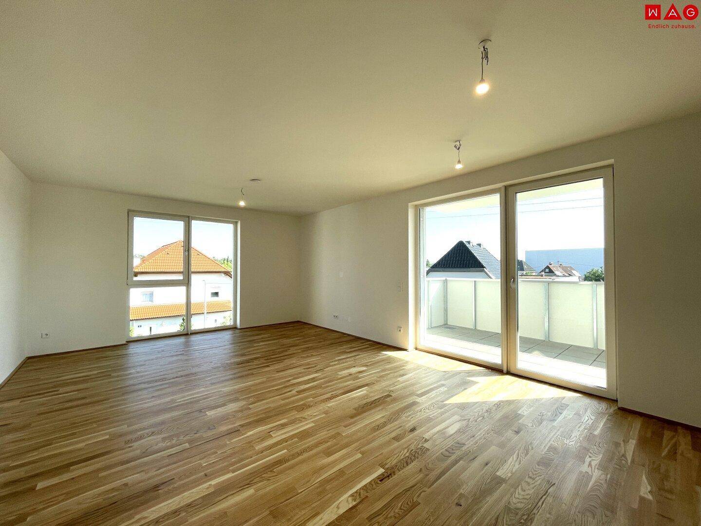Lichtdurchflutetes Wohnzimmer mit Holzboden und Zugang zu einem sonnigen Balkon.