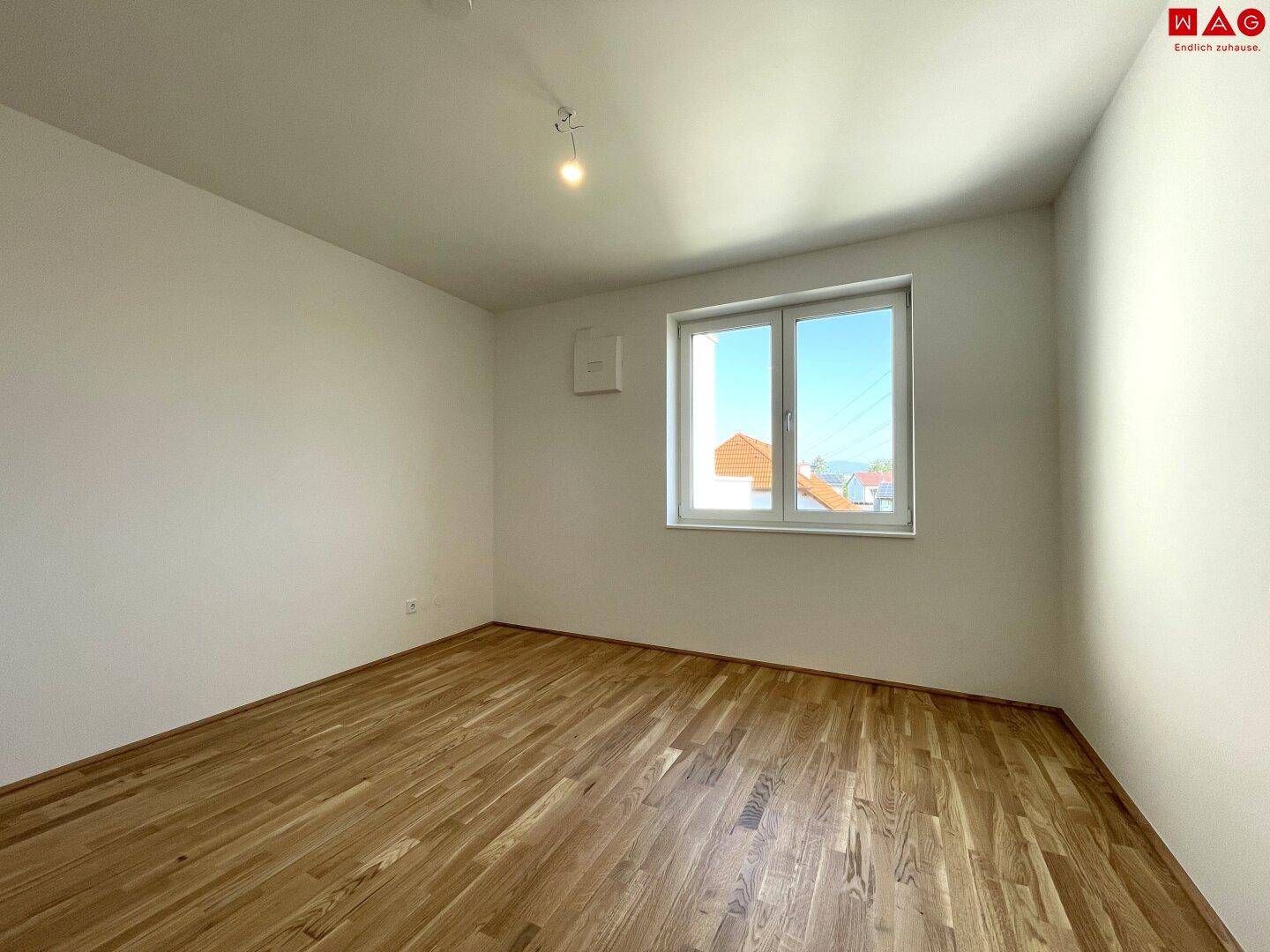 Geräumiges Schlafzimmer mit Holzboden und großem Fenster, das viel Tageslicht bietet.