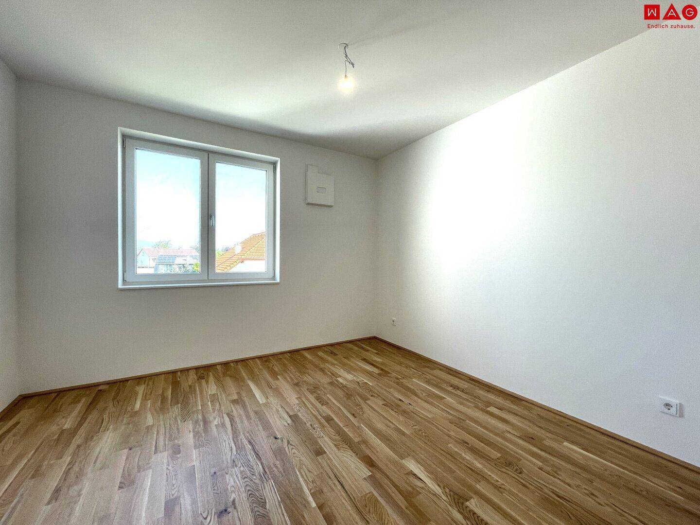Helles Schlafzimmer mit Holzboden und großem Fenster, bereit zur individuellen Gestaltung.