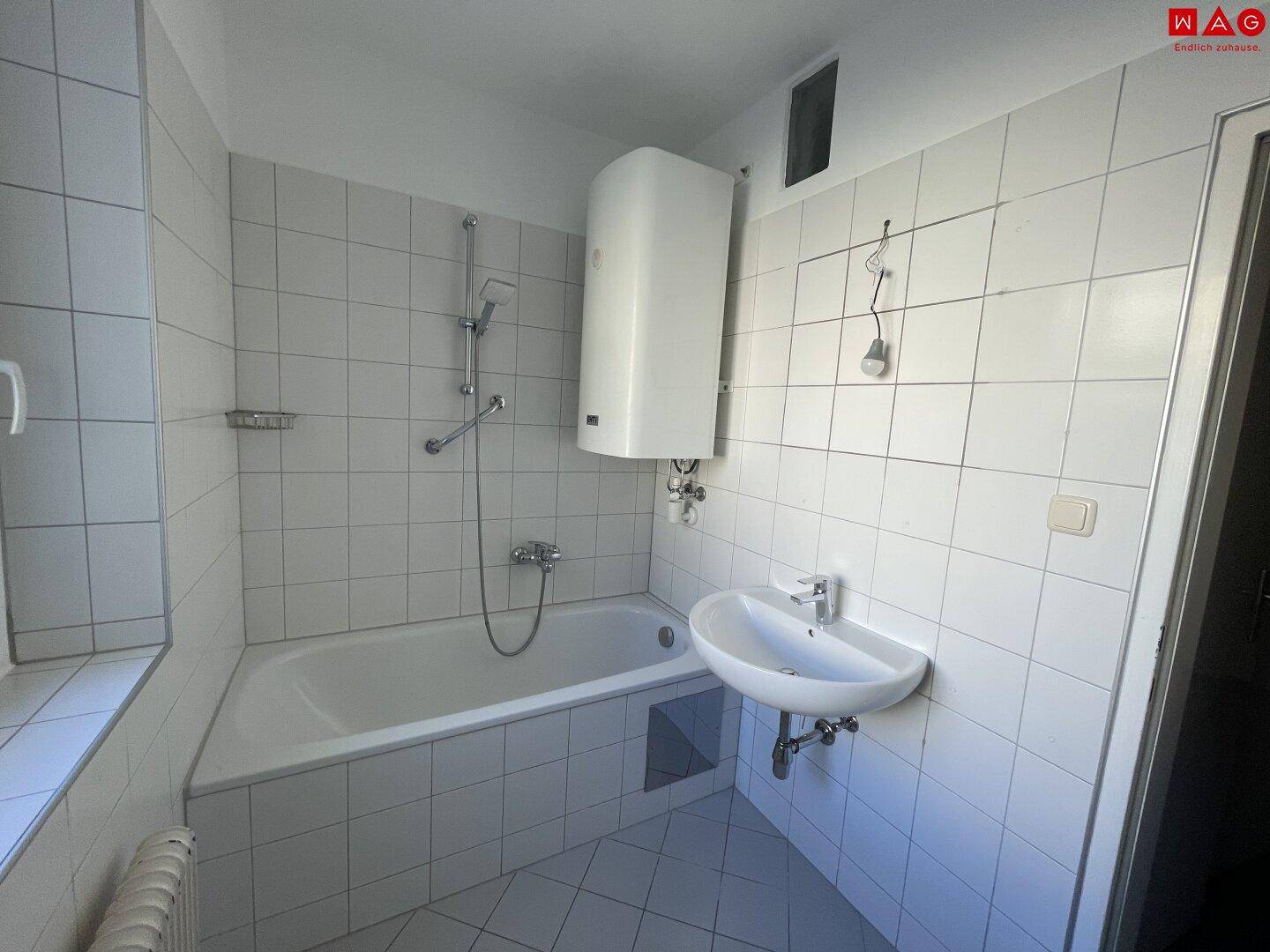Funktionales Badezimmer mit Badewanne, Waschbecken, weißen Fliesen und Fenster.