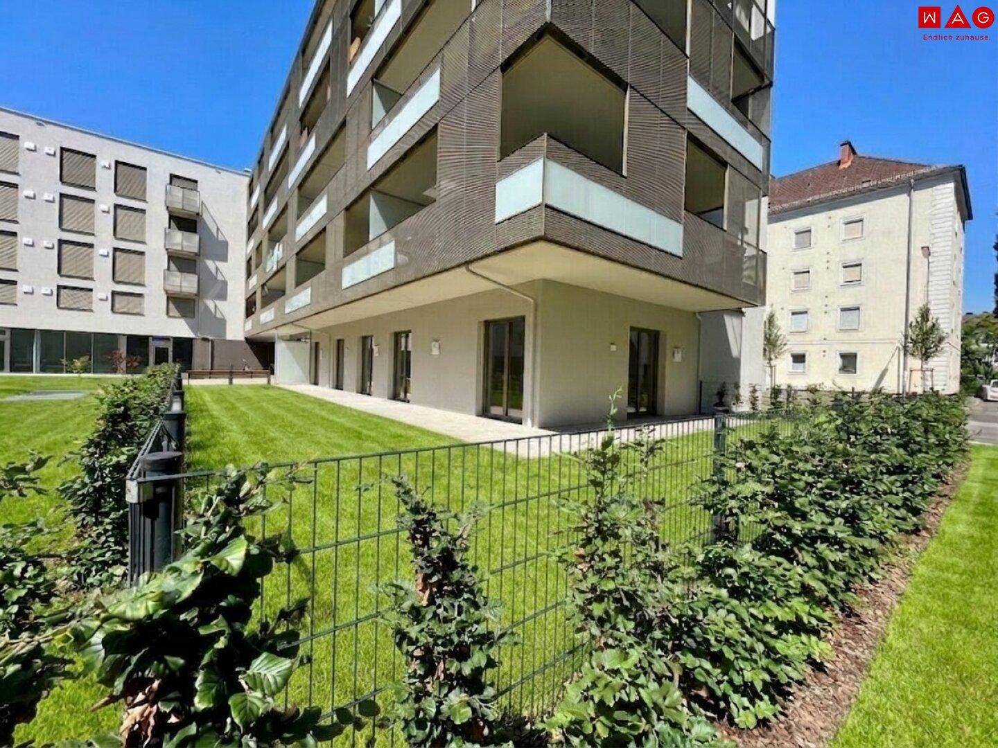 Außenansicht eines modernen Wohngebäudes mit grüner Gartenanlage und Hecken.
