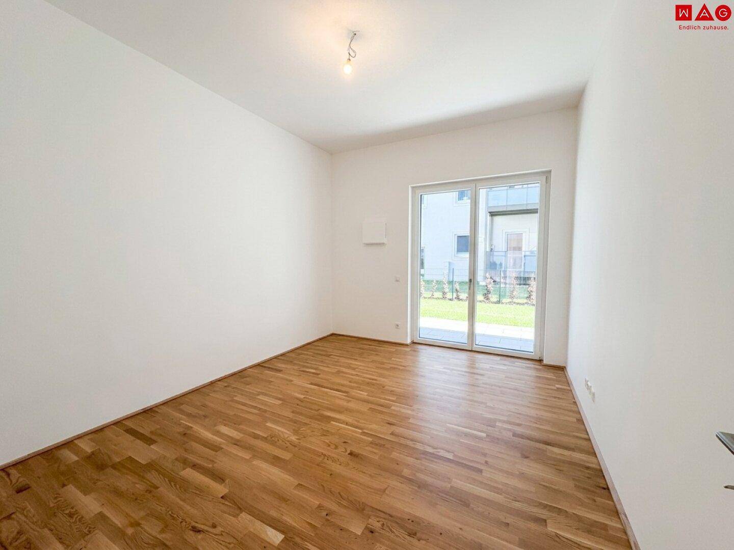 Helles Zimmer mit Holzboden und Zugang zu einem Außenbereich durch große Schiebetüren.