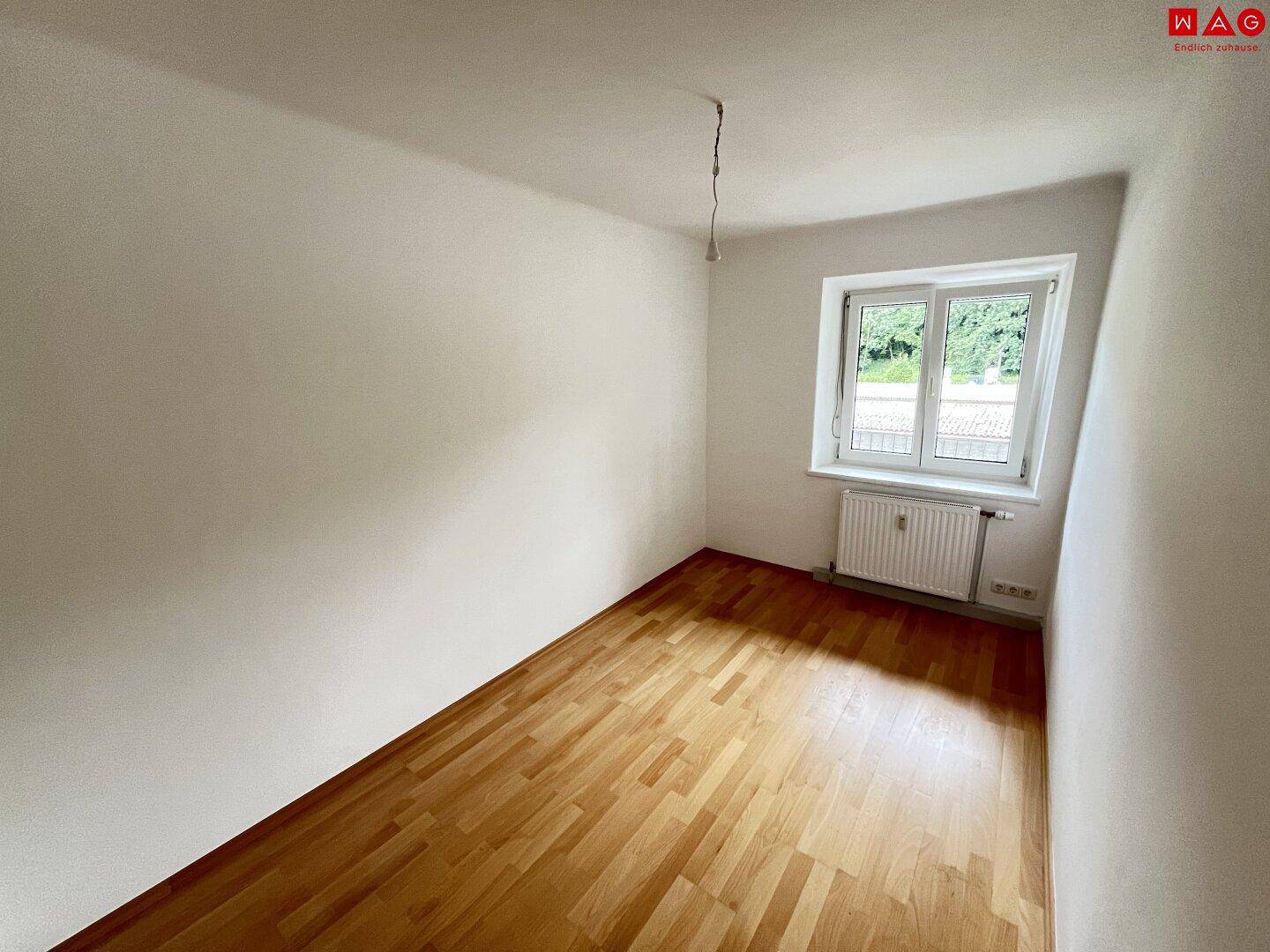 Gemütliches Schlafzimmer mit Laminatboden und einem Fenster zum Grünen.