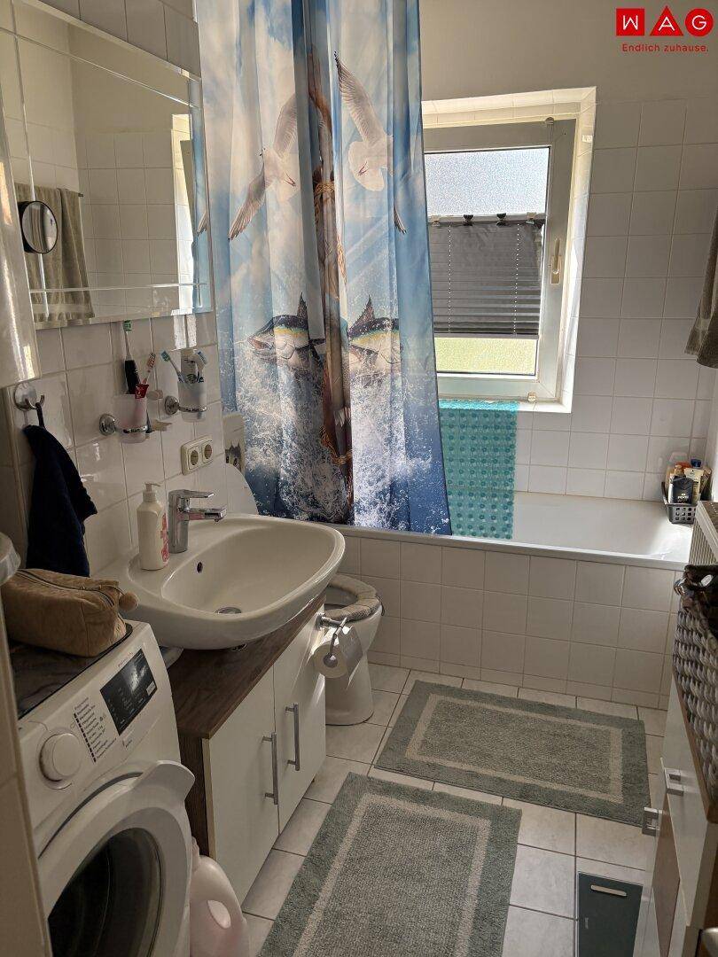 Funktionales Badezimmer mit Badewanne, Waschbecken, WC und Waschmaschine.