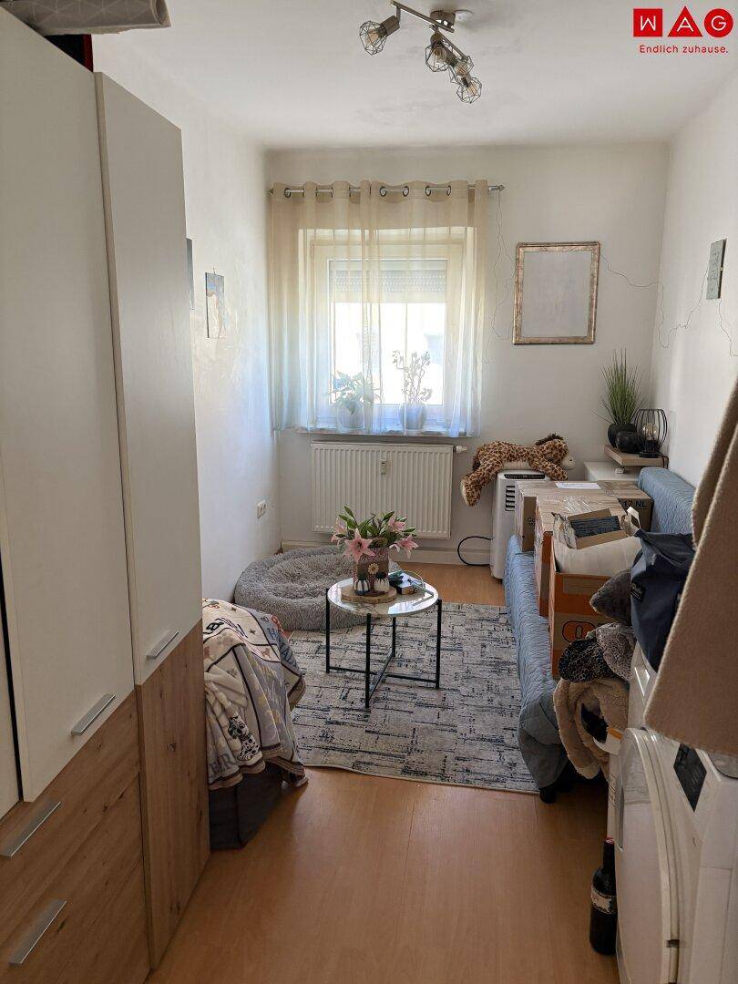 Kleines Schlafzimmer mit Fenster, Laminatboden und einfacher Einrichtung.