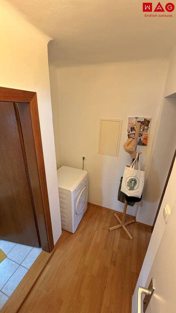 Praktischer Hauswirtschaftsraum mit Waschmaschine und Garderobe auf hellem Holzboden.