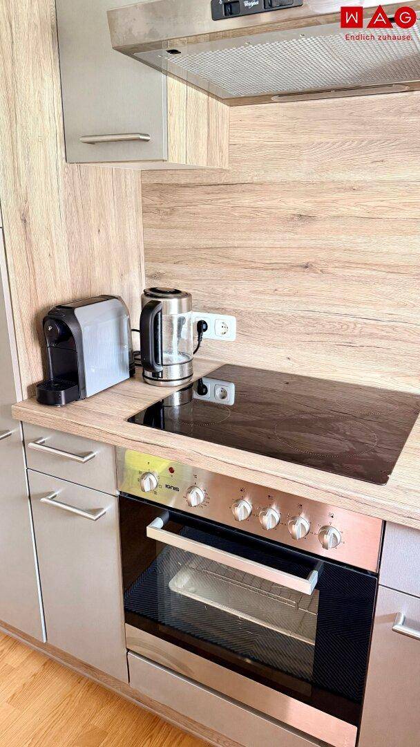 Nahaufnahme der Küchenzeile mit Induktionskochfeld, Backofen, Kaffeemaschine und Wasserkocher auf der Holzarbeitsplatte.