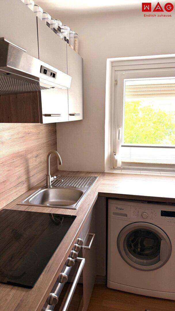 Küchenbereich mit Spüle, Induktionskochfeld und integrierter Waschmaschine unter dem Fenster.