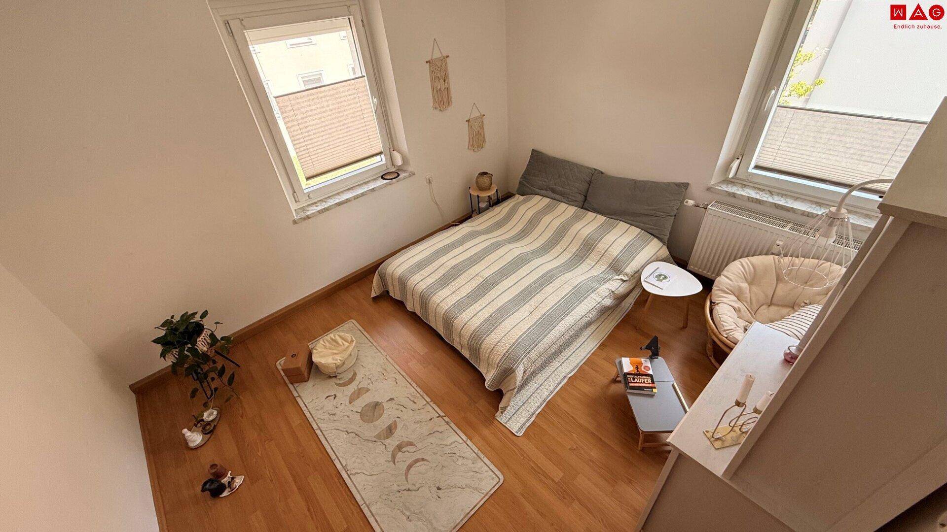 Gemütliches Schlafzimmer mit Holzboden, einem Doppelbett und zwei Fenstern, die viel Licht hereinlassen.