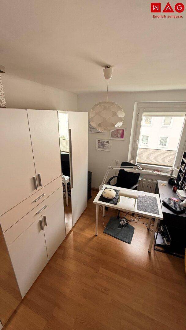 Funktionaler Arbeitsbereich mit Schreibtisch, Bürostuhl und einem großen weißen Kleiderschrank auf Holzboden.