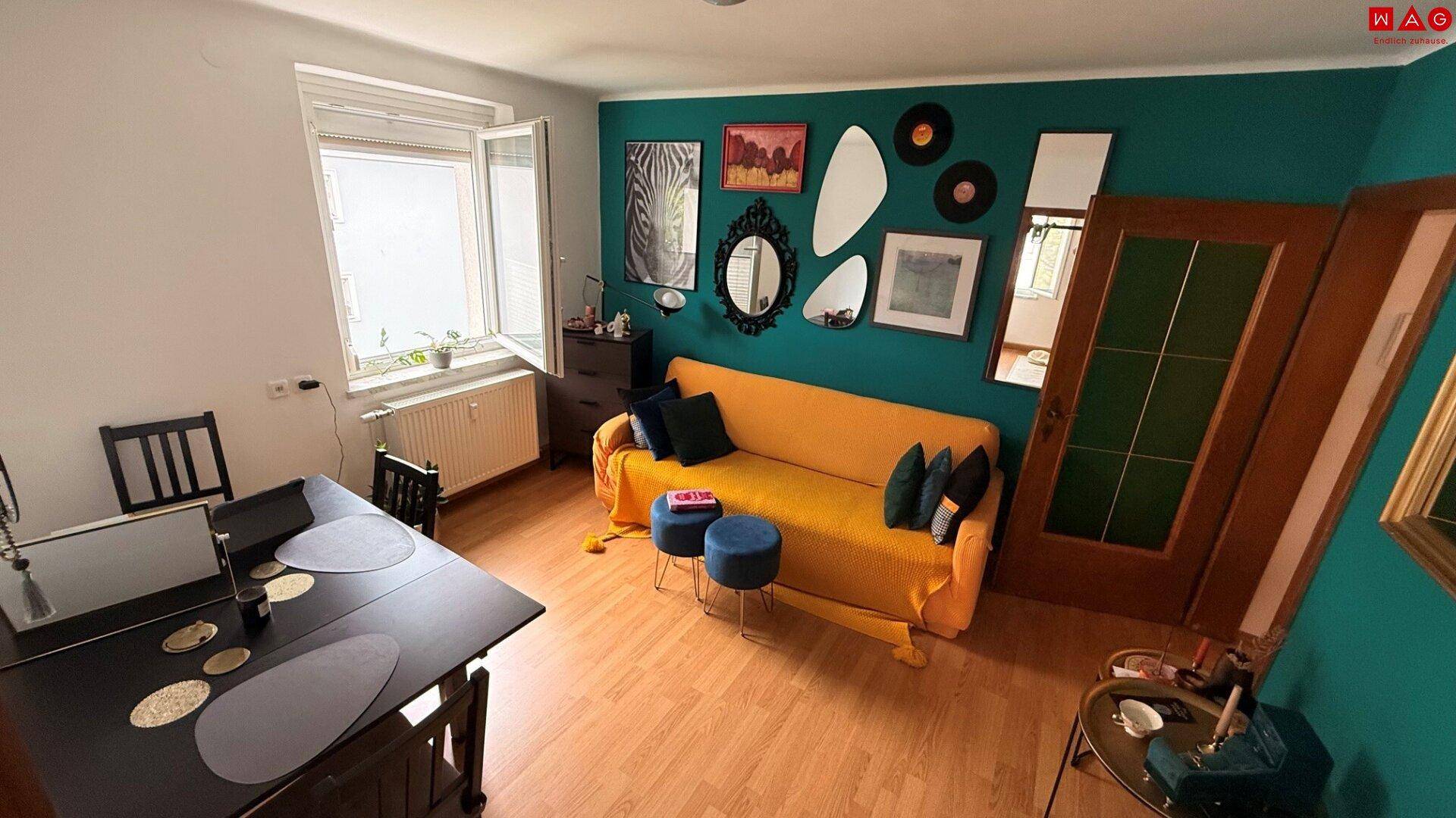 Farbenfroher Wohn-Essbereich mit gelbem Sofa, Esstisch und einer auffälligen türkisfarbenen Akzentwand.