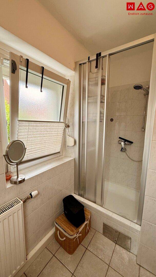 Badezimmer mit Duschkabine, Heizkörper und einem Fenster, das für natürliche Belüftung sorgt.