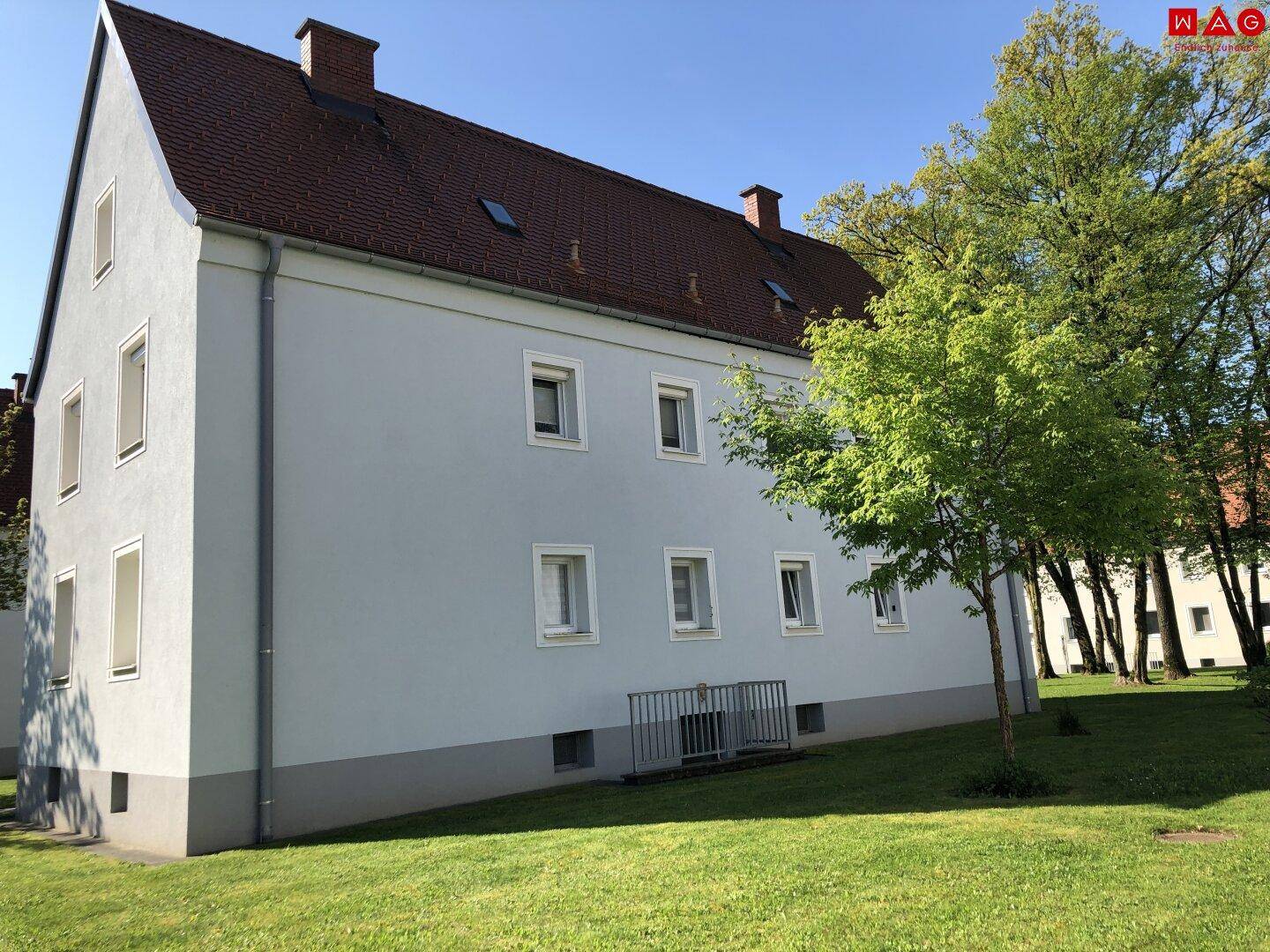 Seitenansicht des Wohngebäudes mit hellblauer Fassade, rotem Dach und umliegender Grünfläche.