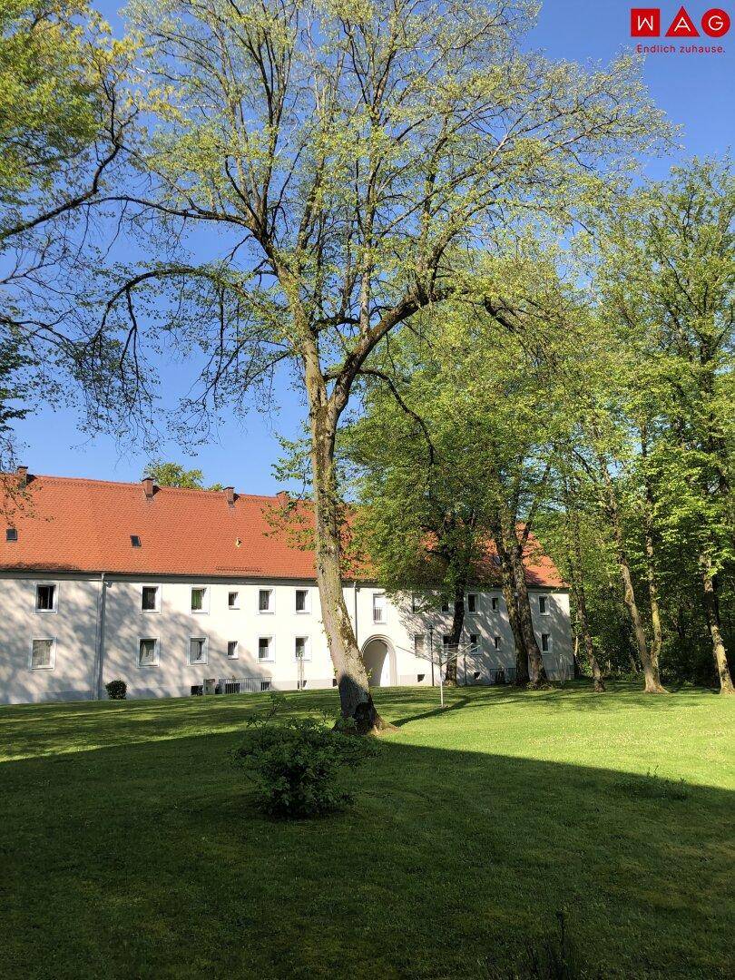 Wohnanlage mit mehreren Gebäuden, umgeben von großen Bäumen und weitläufigen Grünflächen.