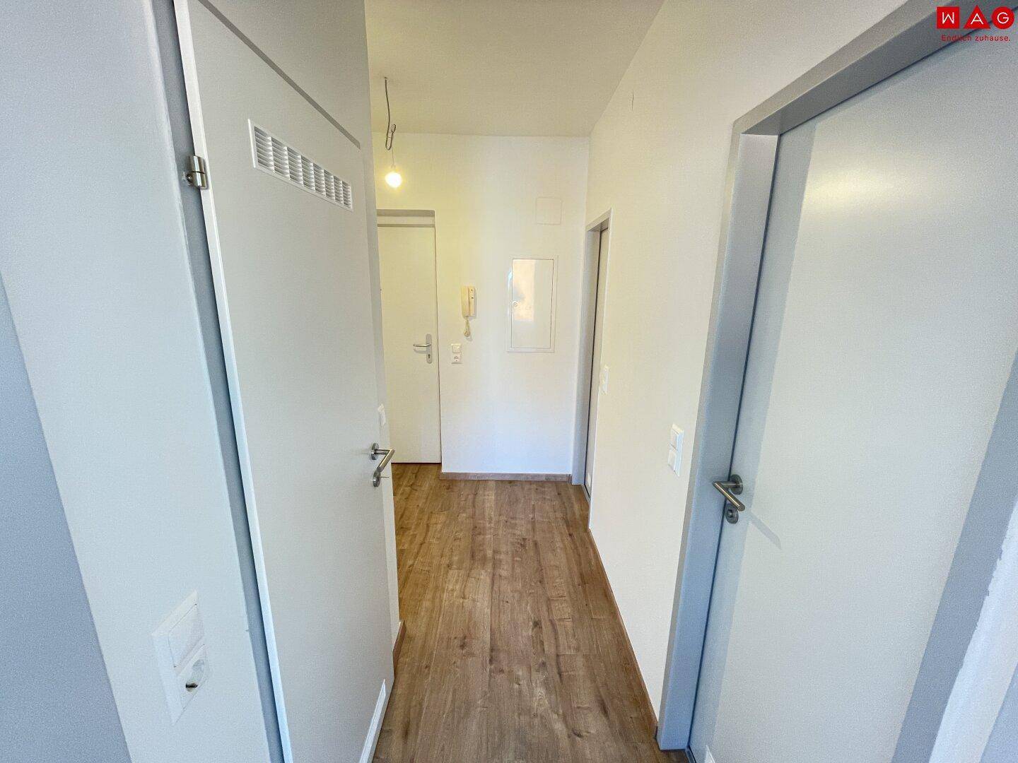 Heller Flur mit Laminatboden, weißen Wänden und mehreren Türen.