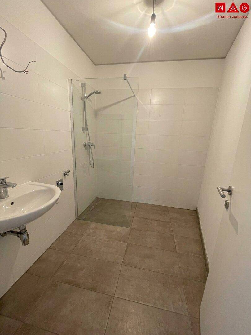 Modernes Badezimmer mit ebenerdiger Dusche und weiß gefliesten Wänden, funktional und hell.