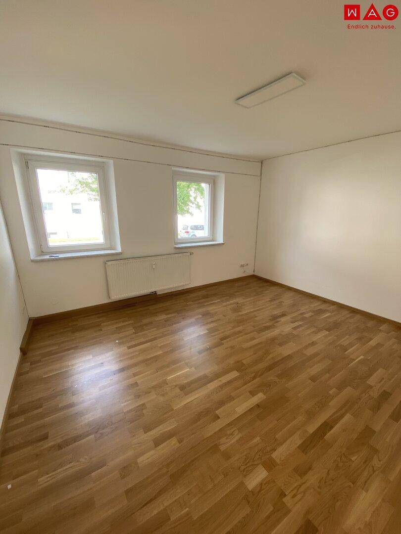 Geräumiges Wohnzimmer mit Holzparkettboden und Blick ins Grüne durch die Fenster.