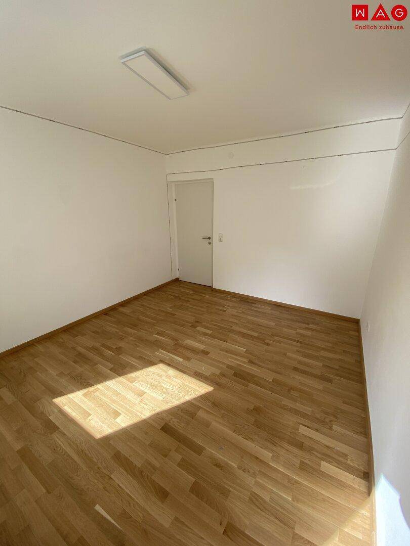Leeres Wohnzimmer mit Holzparkettboden und weißer Tür, bereit für die individuelle Gestaltung.