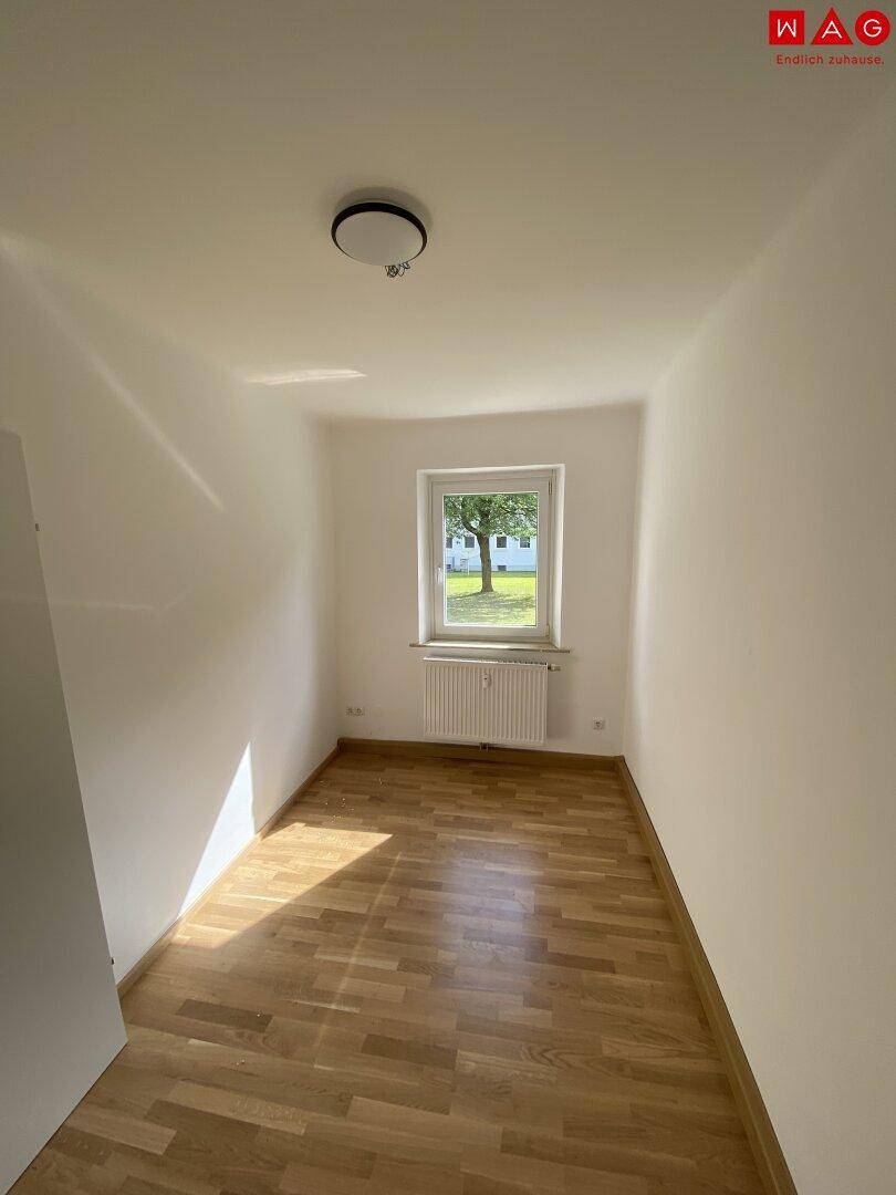 Kleines Schlafzimmer mit Holzparkettboden und einem Fenster, das viel Tageslicht bietet.