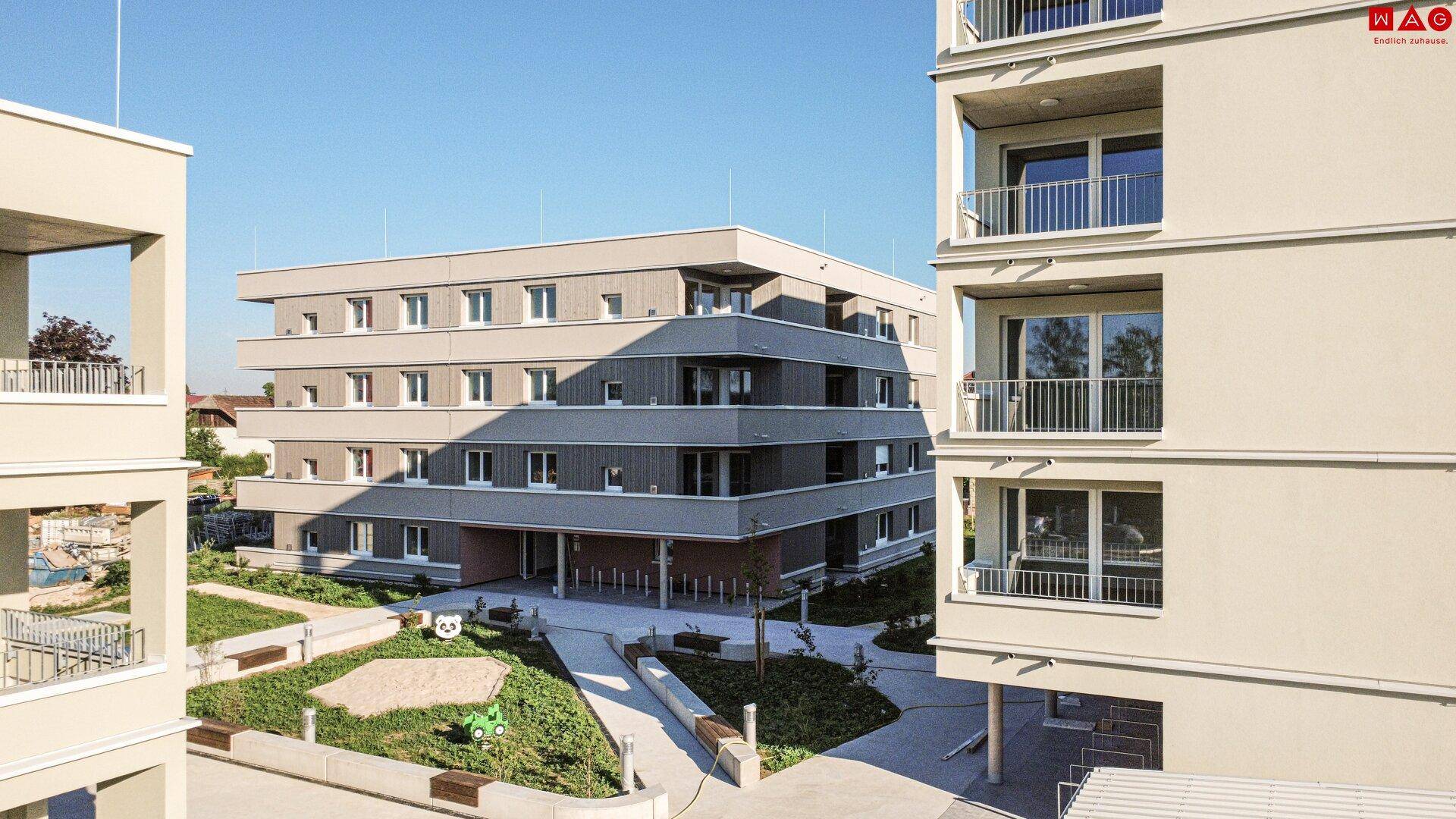 Moderne Wohnanlage mit mehreren Gebäuden und einem begrünten Innenhof mit Spielplatz.