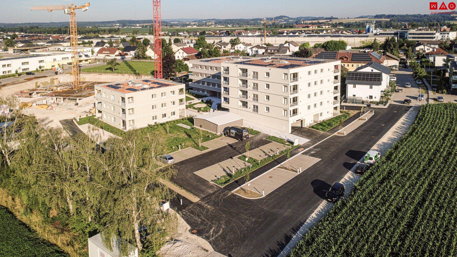 Luftaufnahme von modernen Neubauten mit Solaranlagen, umgeben von Feldern und einer Baustelle.