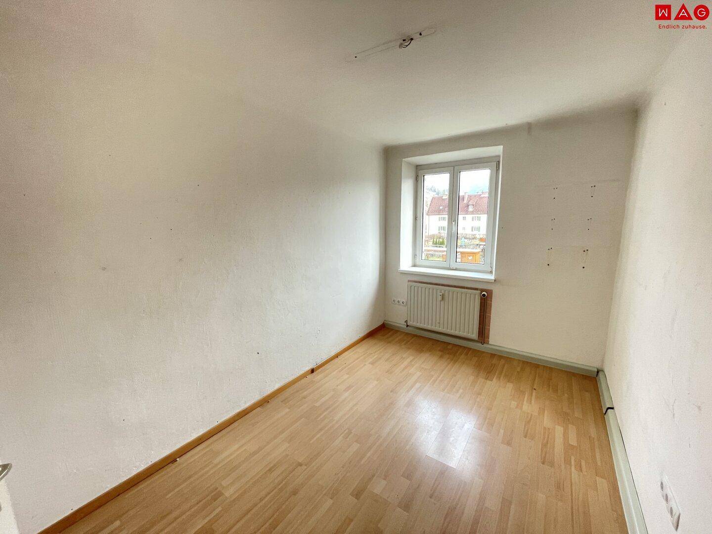 Heller, leerer Raum mit Parkettboden, Fenster und Blick ins Grüne, ideal für Schlaf- oder Wohnzimmer.