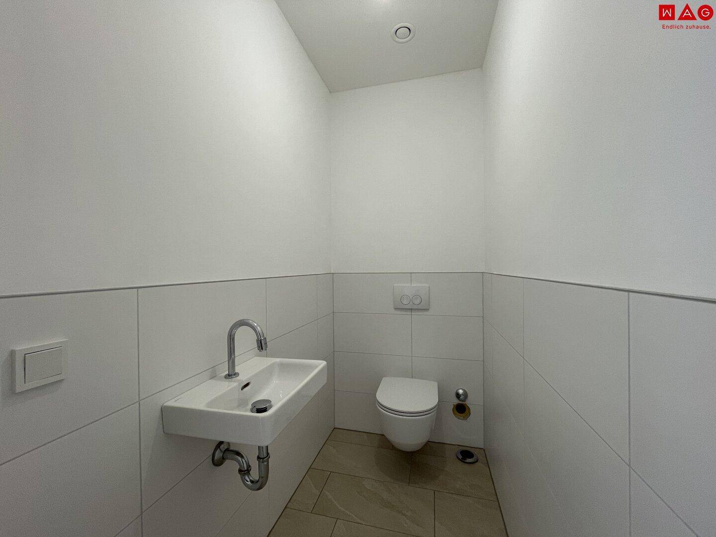 Leeres Gäste-WC mit wandhängender Toilette und modernem Waschbecken.