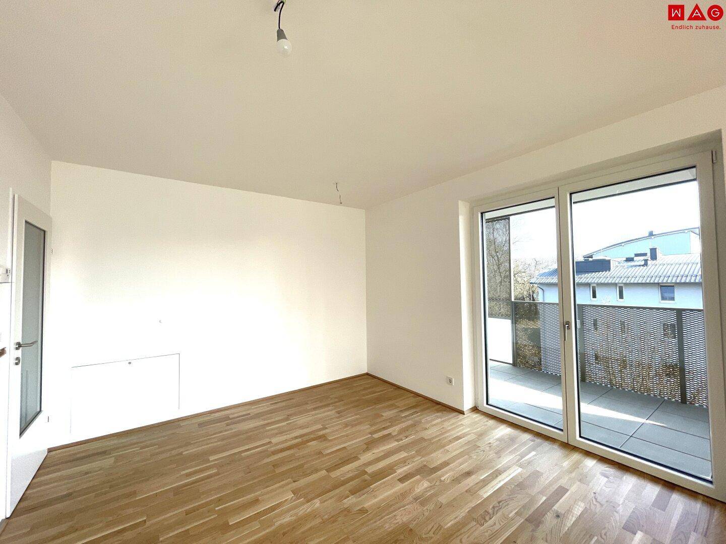 Leerer, heller Raum mit Parkettboden und großen Schiebetüren, die auf eine Terrasse führen.