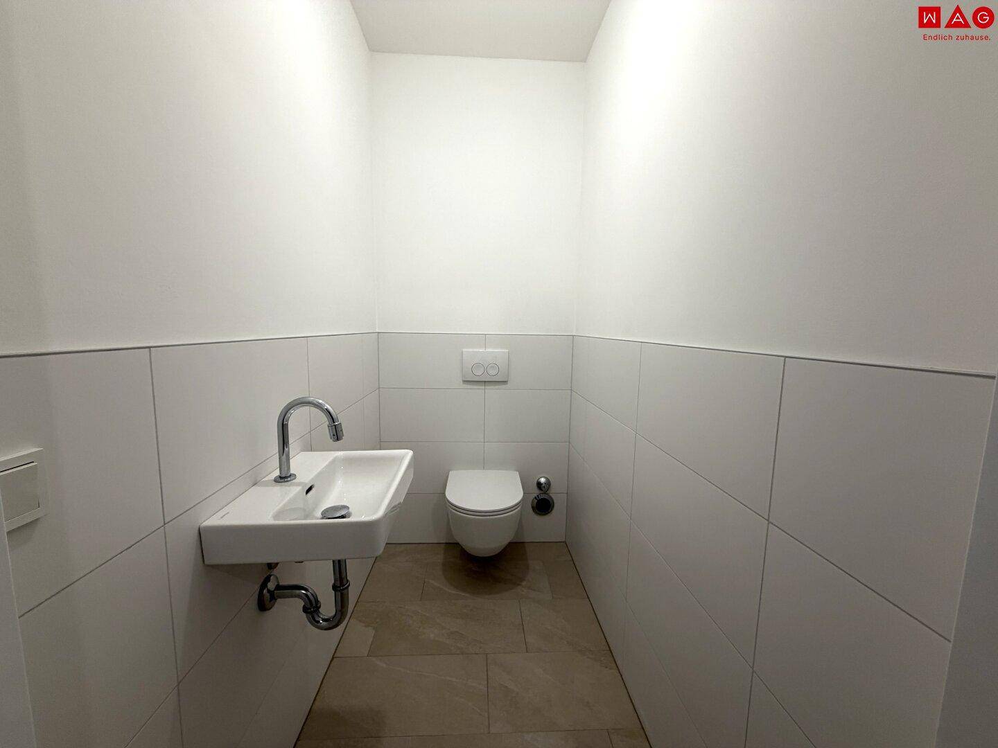 Helles Gäste-WC mit wandhängendem WC, modernem Waschbecken und weißen Wandfliesen.