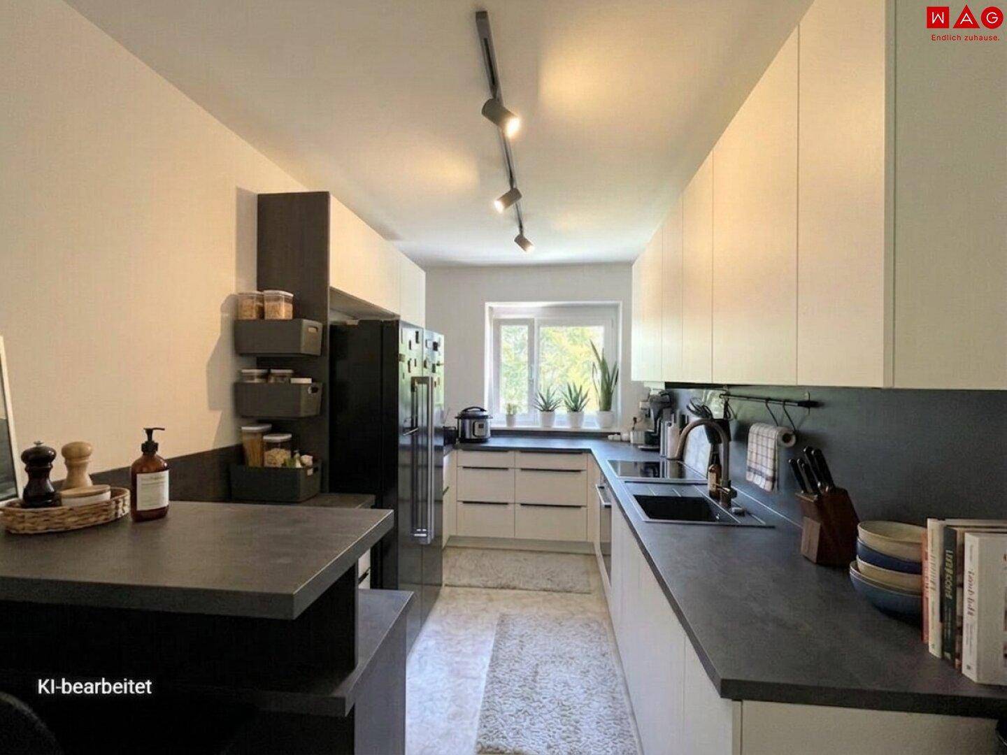 Moderne Küche mit dunklen Arbeitsplatten, weißen Schränken und Fensterblick ins Grüne.