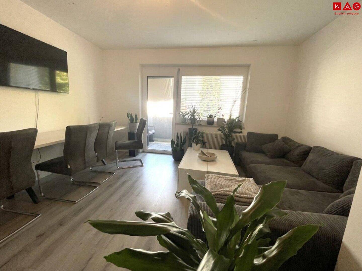 Geräumiges Wohnzimmer mit großem Sofa, Fernseher und Zugang zu einem Balkon.