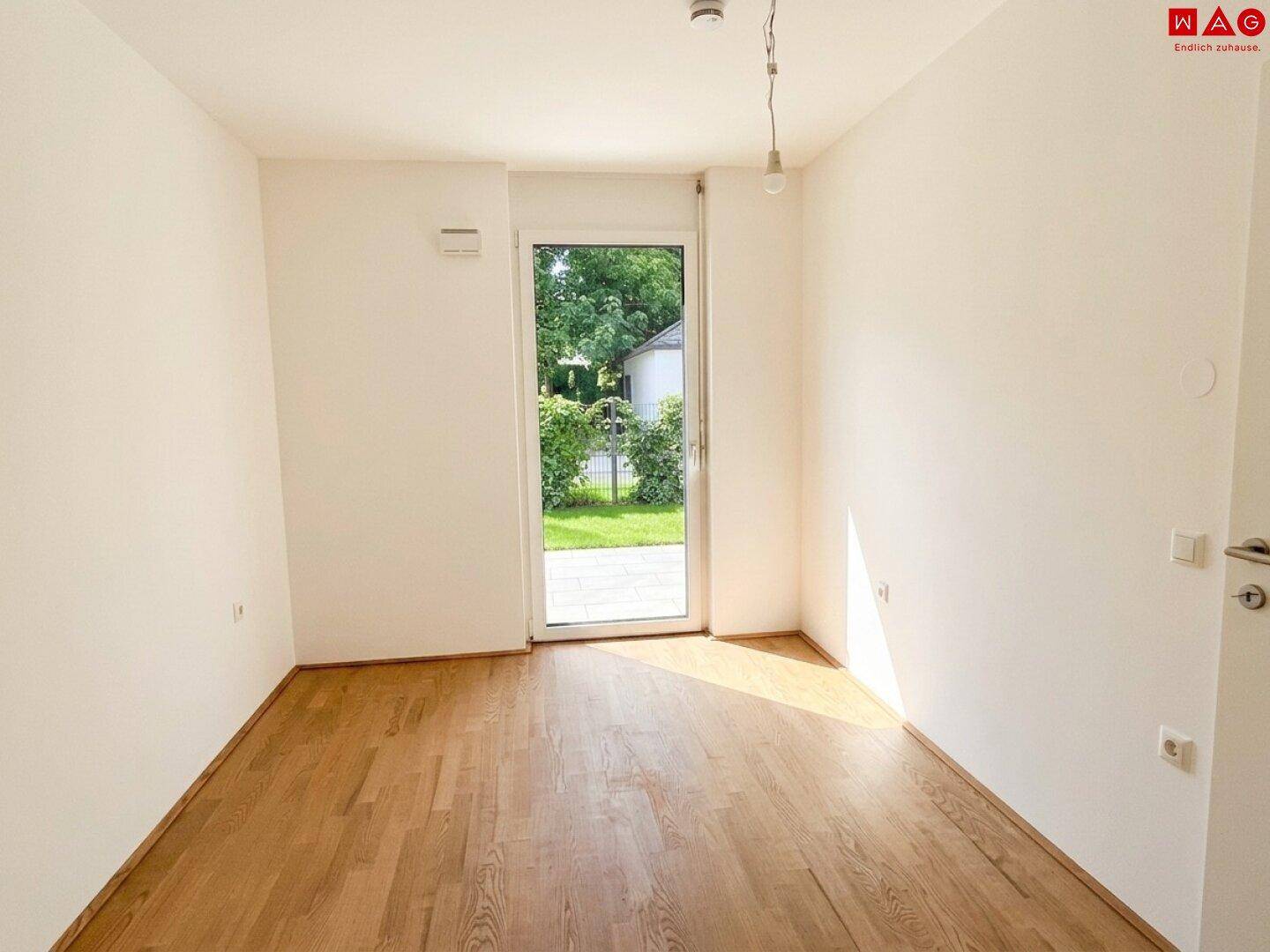 Heller Raum mit Parkettboden und Zugang zu einer Terrasse oder einem Gartenbereich.