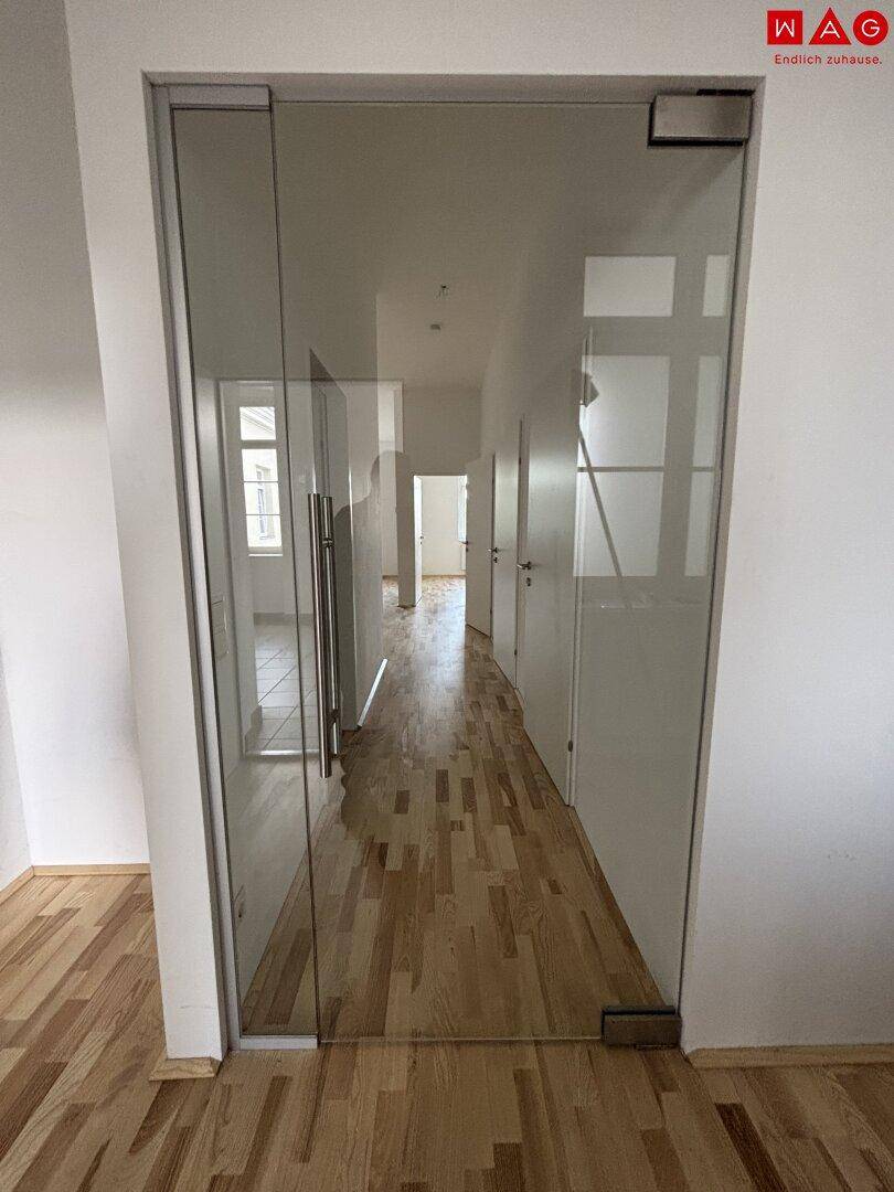 Geräumiger Flur mit hellem Parkettboden und einer eleganten Glastür, die den Blick freigibt.