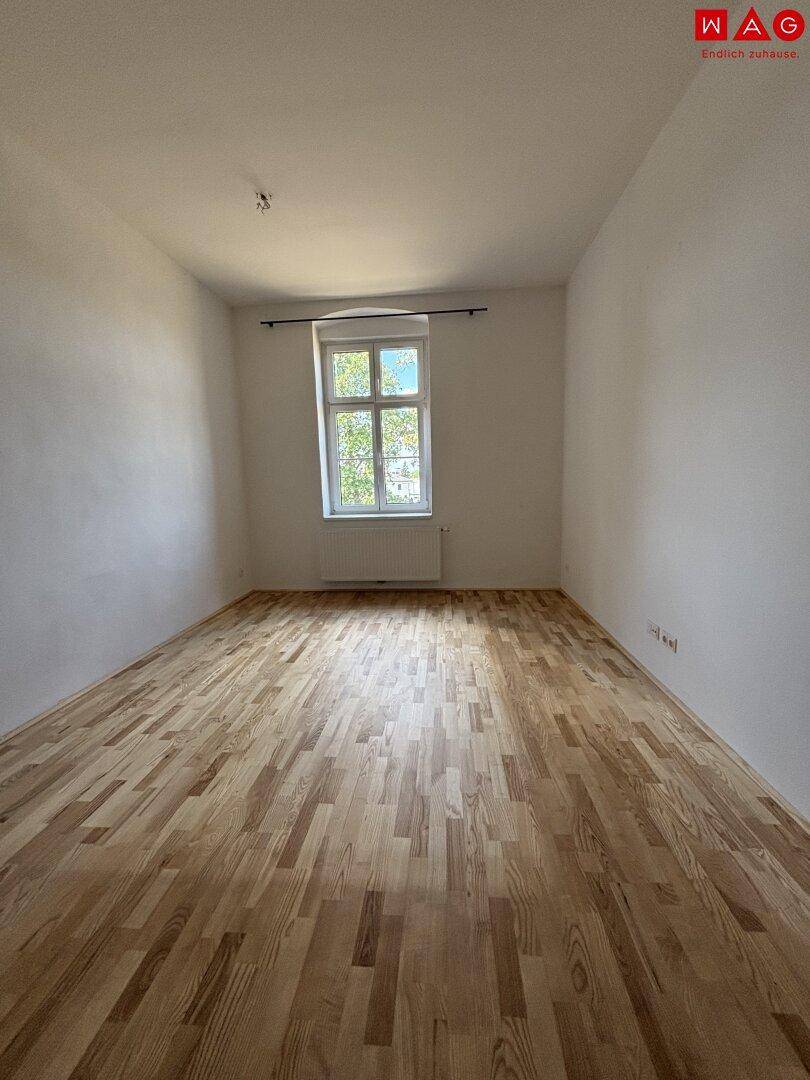Helles Schlafzimmer mit Parkettboden und einem Fenster, das eine angenehme Atmosphäre schafft.