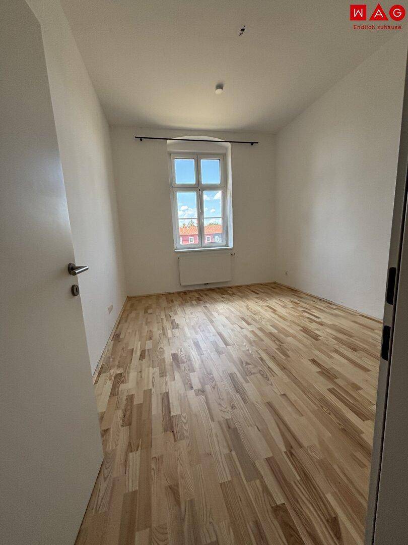 Geräumiges Schlafzimmer mit hellem Parkettboden und einem Fenster, das den Raum gut belichtet.