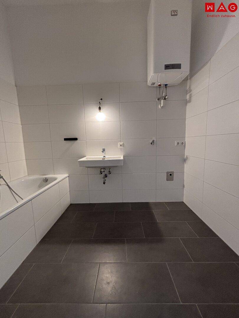 Funktionales Badezimmer mit Badewanne, Waschbecken und einem Warmwasserbereiter an der Wand.