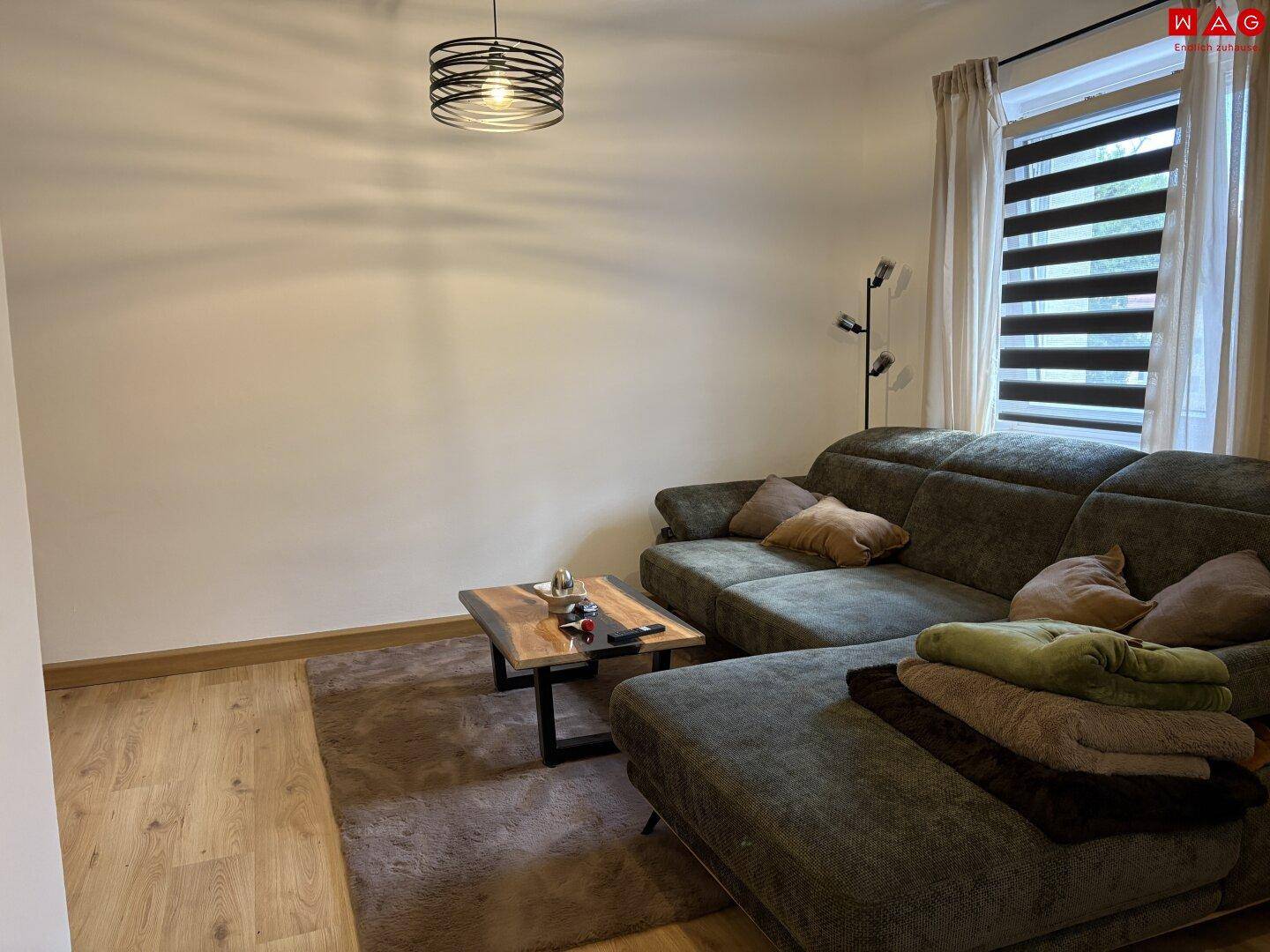 Gemütlicher Wohnbereich mit großem Ecksofa, Couchtisch und weichem Teppich auf dem Holzboden.