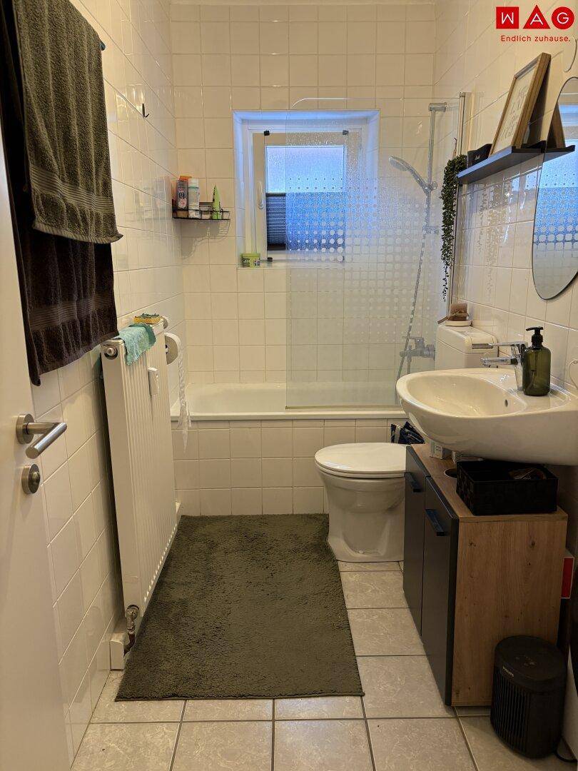 Helles Badezimmer mit Badewanne, integrierter Dusche, Waschbecken und einem Fenster.