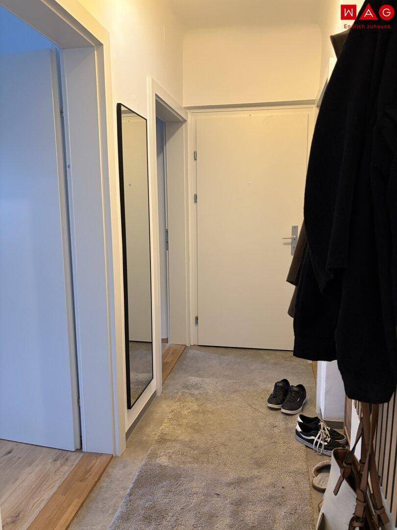 Heller Eingangsbereich mit Garderobe, großem Spiegel und Teppichboden.