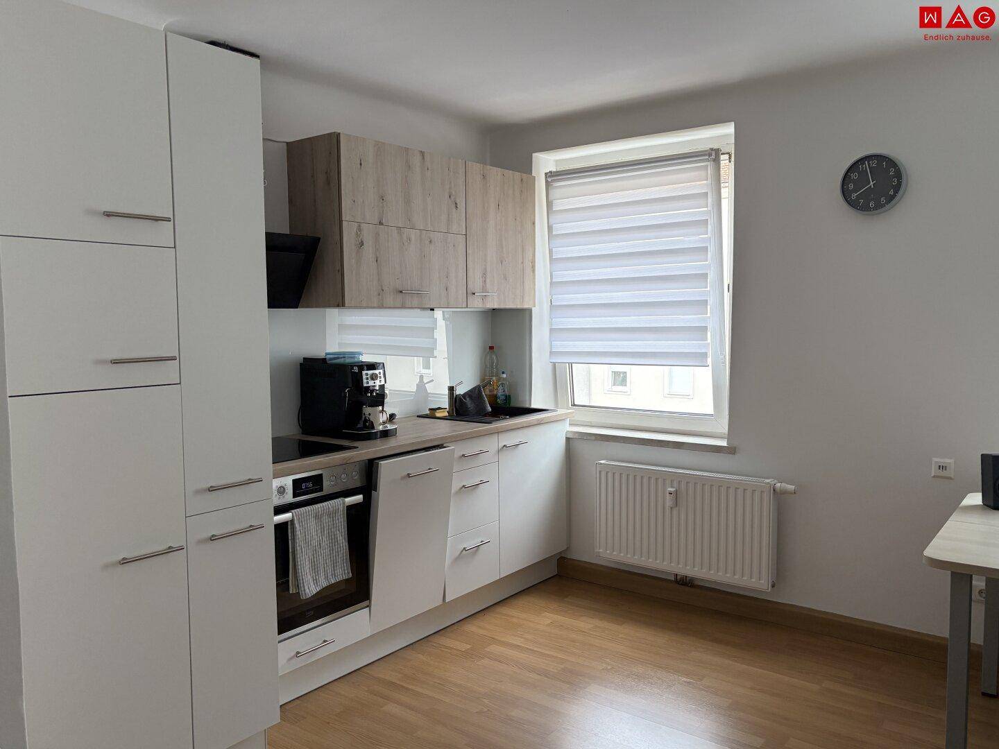 Moderne Küche mit hellen Schränken, integriertem Backofen und Induktionskochfeld.