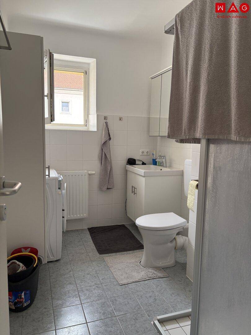 Funktionales Badezimmer mit Dusche, WC, Waschbecken und Fenster, hell gefliest.
